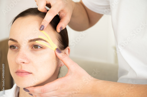 Close-up of cosmetologist making taping face procedure using yellow tapes. Anti-aging treatment against wrinkles.