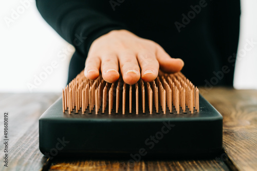 a sadhu board made of dark oak with copper nails on a wooden table. the girl runs her fingers over the copper nails. the yogic practice of standing on nails
