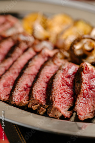 Marbled beef ribeye steak with grilled vegetable garnish, iron tray, wooden table. close up