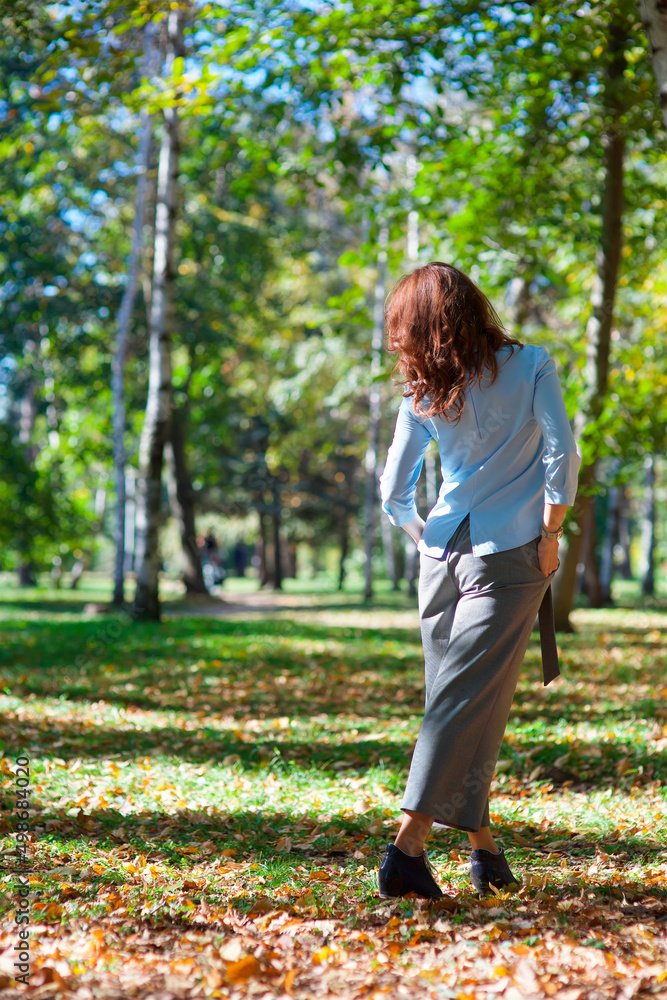A girl with red hair in a cheerful mood walks through the autumn park. The weather is warm.