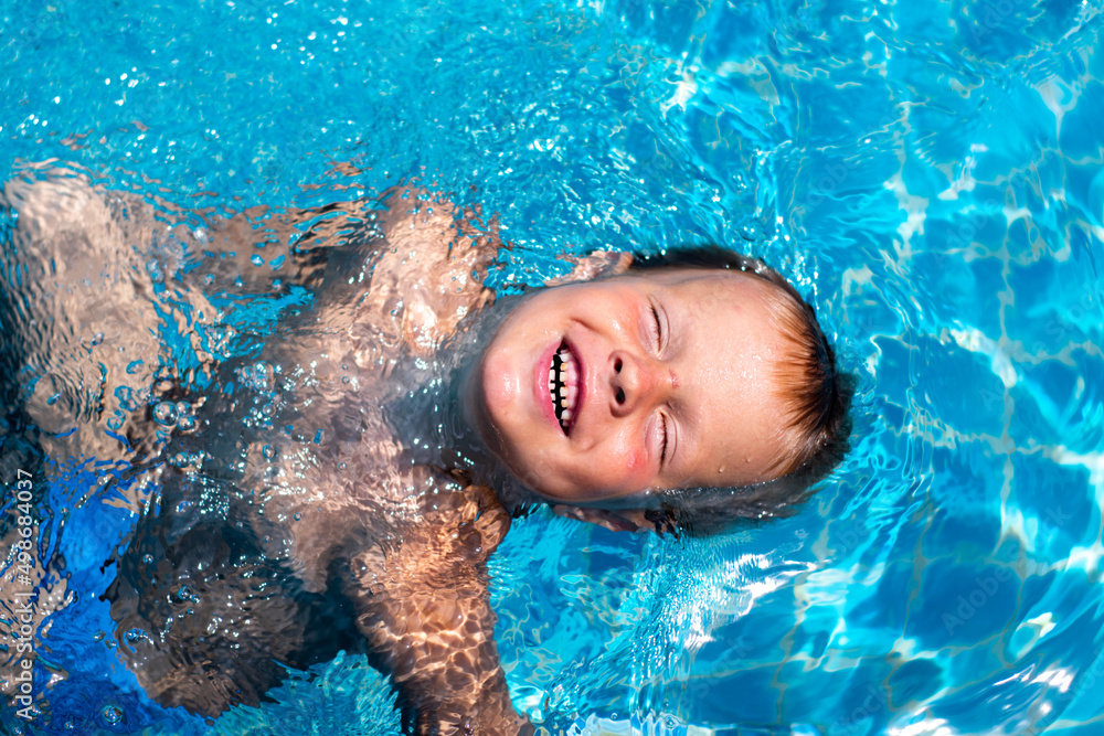 A happy child in the pool. A boy swims in the blue water of the pool on his back. Summer holidays, family travel, rest and relaxation