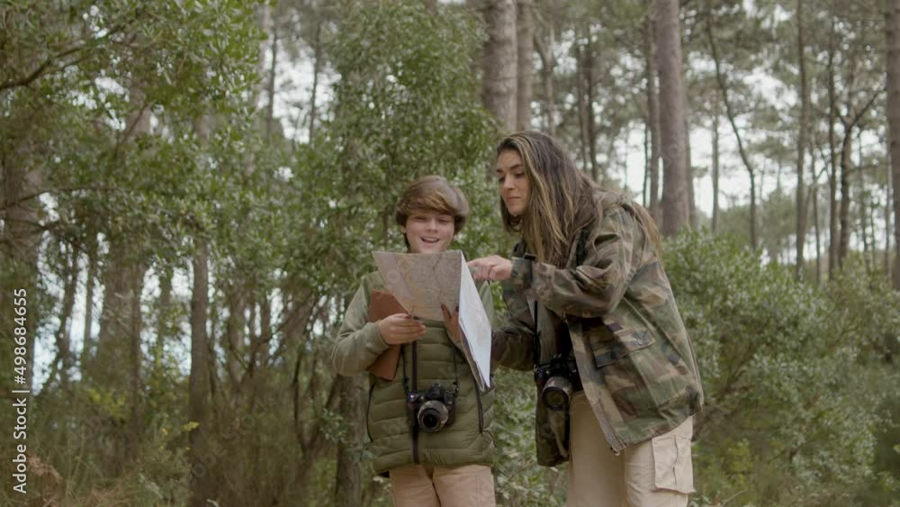 Beautiful woman and her curious son exploring wildlife in forest on autumn day. Smart boy and his mum finding their way, looking at paper map, then woman showing direction. Nature, discovery concept Beautiful woman and her curious son exploring wildlife in forest on autumn day. Smart boy and his mum finding their way, looking at paper map, then woman showing direction. Nature, discovery concept