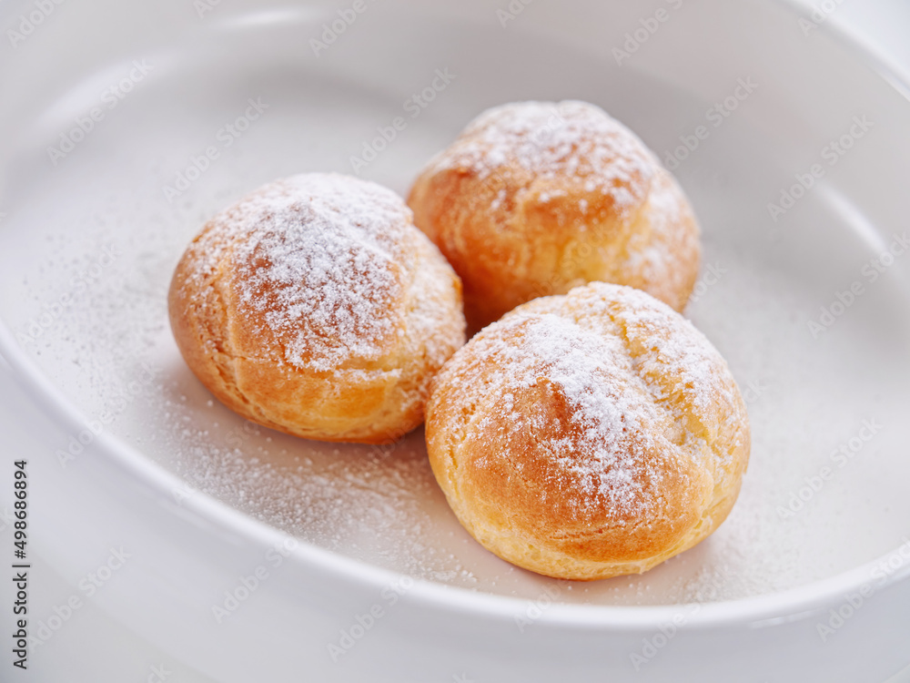 Custard cakes covered with powdered sugar on a white plate. Close-up. Selective focus. Horizontal. High key. White background.	