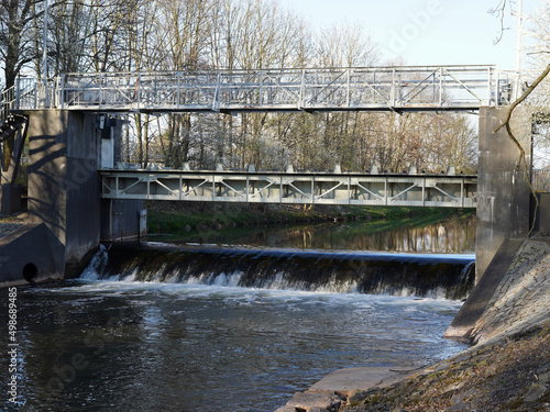 Big weir on the river. Water flows in a stream. We see the iron structure of the weir and the bridge over the river.
