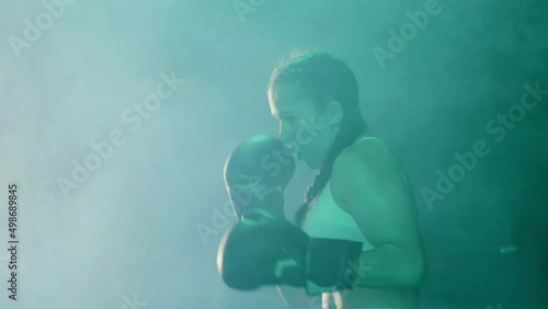 Young female boxer doing shadow fight, practicing right uppercut punch. Sporty girl with pigtails and kappa in her mouth wearing boxing gloves and training alone. Boxing, sports concept photo