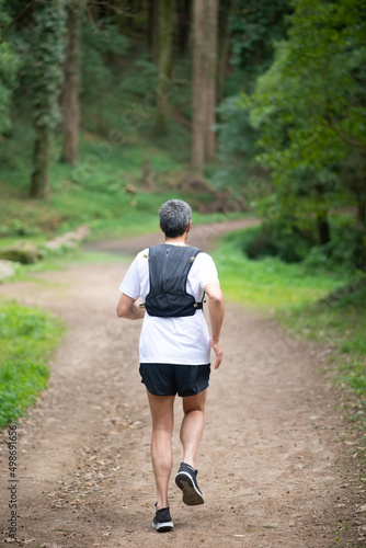 Back view of man jogging in forest. Sporty person in sportive clothes exercising outdoors. Sport, hobby concept