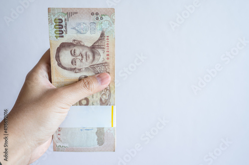 Valokuvatapetti Someone hand holding a pile of one thousand Thai baht banknotes isolated on white background