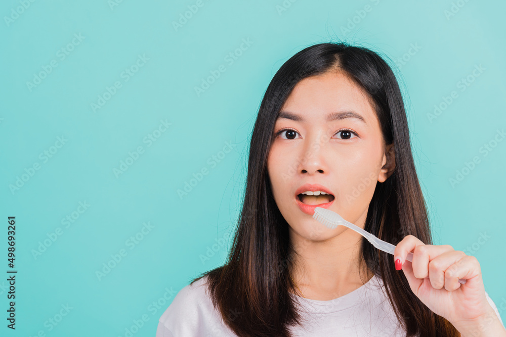 Asian beautiful young woman teen brushing teeth in the morning, portrait of happy Thai female confident smiling holding toothbrush, studio shot isolated on blue background, Dental health concept Asian beautiful young woman teen brushing teeth in the morning, portrait of happy Thai female confident smiling holding toothbrush, studio shot isolated on blue background, Dental health concept