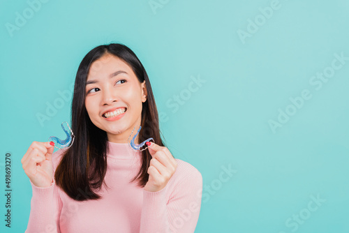 Portrait Asian beautiful young woman smiling hold silicone orthodontic retainers for teeth, Teeth retaining tools after removable braces, isolated blue background, Dental hygiene healthy care concept photo