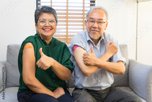 Konstfotografi Senior Asian couple get vaccinated with bandage on arm show thumb up sign in living room