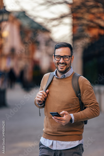 Fototapeta Portrait of happy caucasian man with glasses, holding his phone, sightseeing