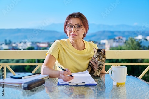 Middle aged woman with pet cat looking at webcam talking online recording video