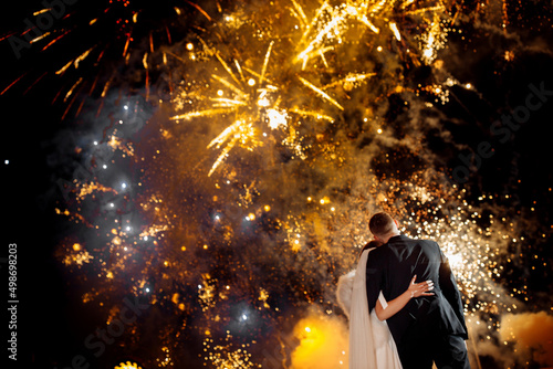 Wedding fireworks. Back view of bride and groom hugging in the night on firework and salute background on night sky, enjoying the happiest day in life