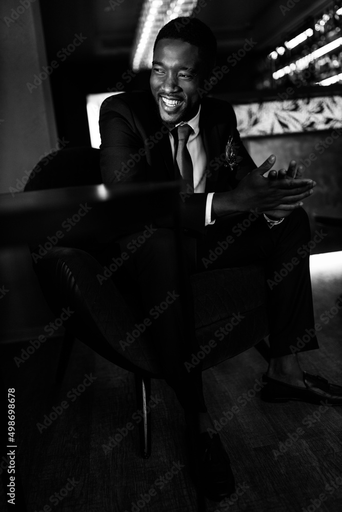 Successful business man sit in a bar, planing new deal or project, smiling. Handsome African American male boss show confidence and success. Influential leader of company wearing stylish formal suit