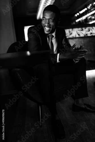 Successful business man sit in a bar, planing new deal or project, smiling. Handsome African American male boss show confidence and success. Influential leader of company wearing stylish formal suit