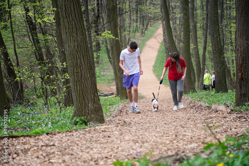 A young girl and a boy are walking through the forest with their dog