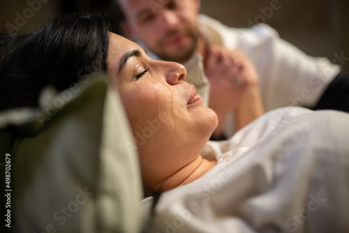 Crying woman giving birth at home. Woman with pierced nose lying, feeling contractions during childbirth. Pregnancy, home birth concept