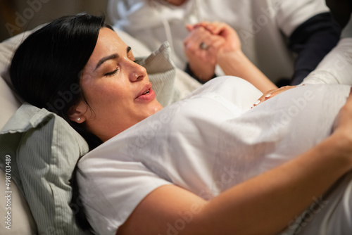 Dark-haired woman giving birth at home. Woman with pierced nose lying, feeling contractions during childbirth. Pregnancy, home birth concept photo