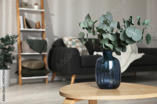 Blue glass vase with beautiful eucalyptus branches on wooden table in living room, space for text photo