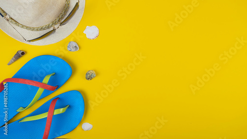 Flip-flops, hat, sunglasses and seashells on yellow background. Top view, space for text