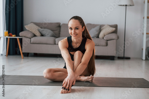 Sitting and smiling. Young woman with slim body type and in yoga clothes is at home