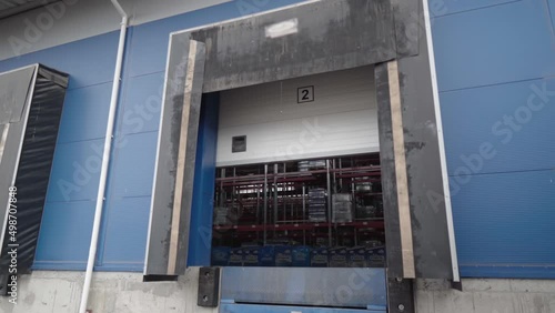 Opening the warehouse door. Large roll-up gates to the enterprise shooting from the street. Roller shutter door of the hangar. Smooth camera movement.