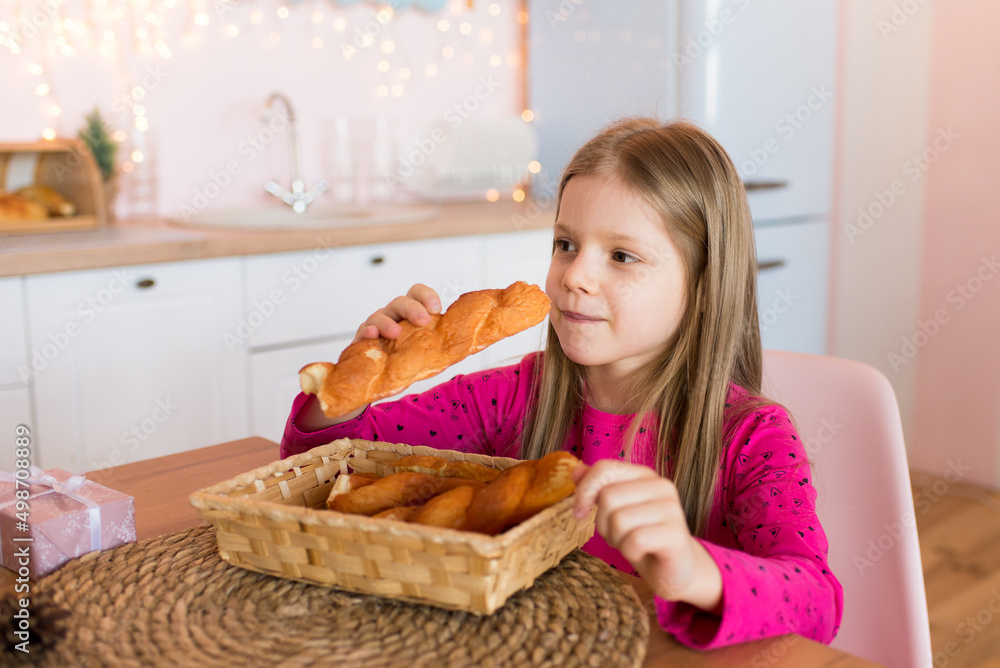 Cute smiling girl holding bread. Sits in the kitchen.

