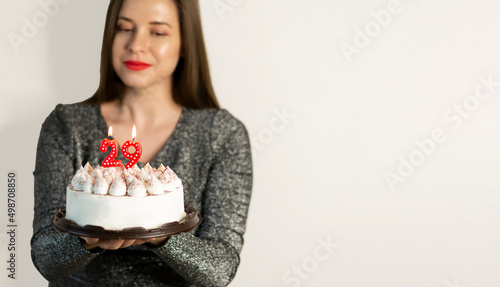 Woman holding birthday cake with candles with the number 29 on light gray background mockup