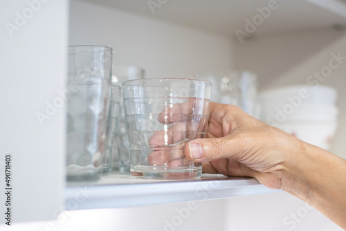 Hand leaving a glass in a cupboard full of glasses in a kitchen. Soft light, bright.