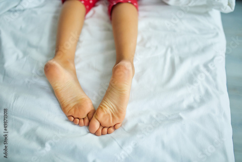 Girl's feet covered with white bed sheet, sleeping in a comfortable bed