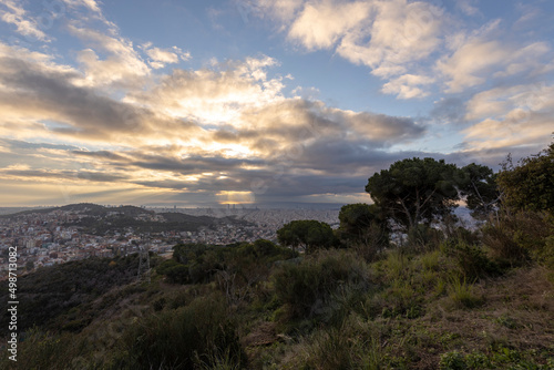 Picturesque landscape of Barcelona from the hill in the early morning. Sunbeams through the clouds. Dramatic sky over the city. Autumn in Barcelona, Spain.