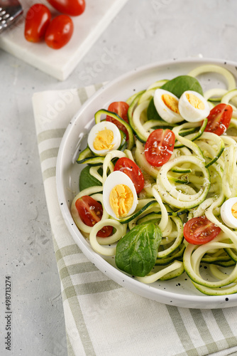 Keto paleo low-carb zoodles: zucchini noodles with parmesan cheese, cherry tomatoes, quail eggs on a checkered kitchen towel light grey surface