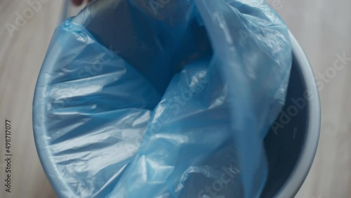 Female hands putting plastic bag in garbage bin at home indoors. Unrecognizable tidy Caucasian young woman cleaning house preparing container for food remains. Close-up