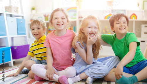 Group of children sitting indoors on the floor and looking in the camera.