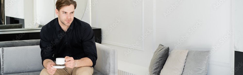 man in black shirt sitting on sofa in living room with coffee cup, banner. man in black shirt sitting on sofa in living room with coffee cup, banner.