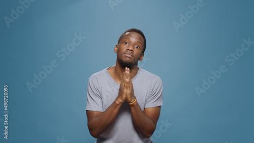 Hopeful man doign prayer gesture with hands in front of camera, begging and imploring for trust and fortune. Wishful person praying and asking for forgiveness, please and apologize pose. photo