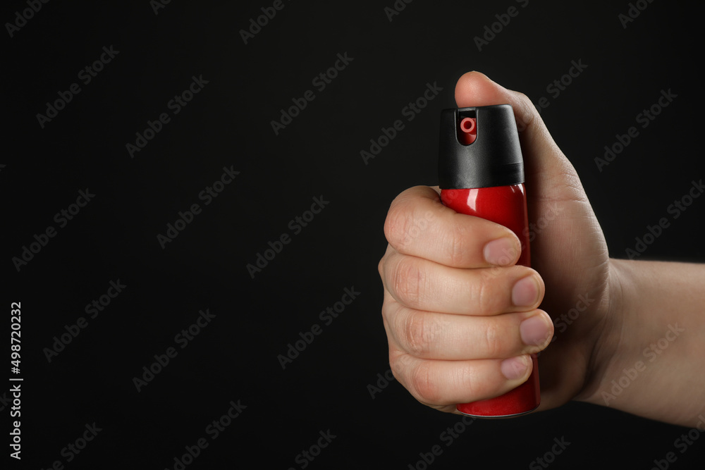 Man holding pepper spray on black background, closeup. Space for text Man holding pepper spray on black background, closeup. Space for text