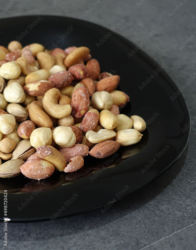 There is a plateful of nuts, hazelnuts, peanuts, cashews in the plate. There is a plateful of nuts, hazelnuts, peanuts, cashews in the plate.