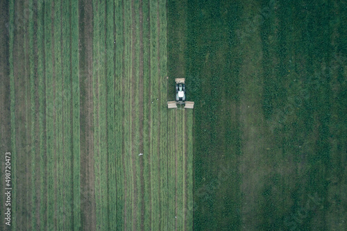 Aerial view of a tractor mowing a green fresh grass field, a farmer in a modern tractor mowing a green fresh grass field