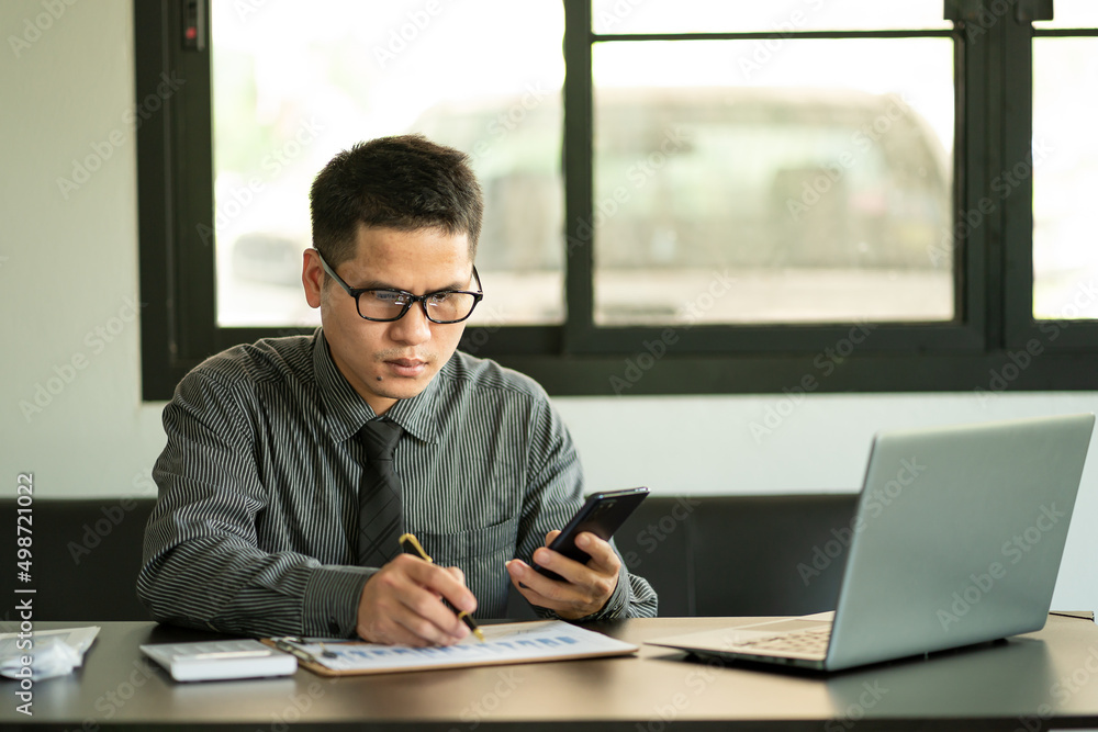 © ArLawKa - Businessman Holding Pen and Smartphone for Calling Marketing Consulting Analyst with Partner With the calculator, laptop, computer, and graph charts for calls. Marketing Consultant