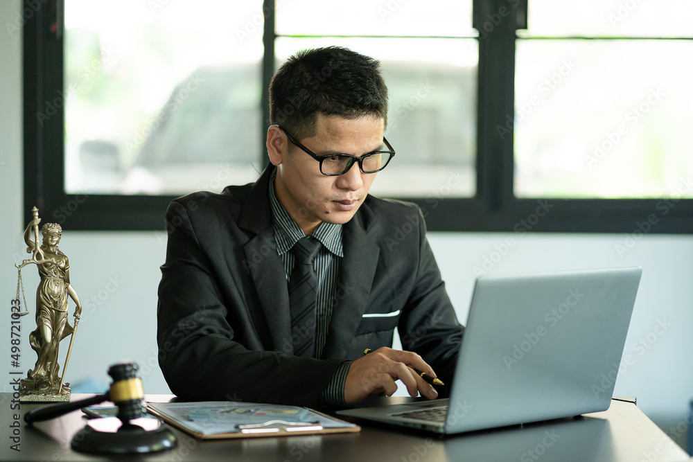 Young Asian lawyer working on laptop, legal contract documents in courtroom, justice and scales hammer, god of justice, legal advisor concept. Young Asian lawyer working on laptop, legal contract documents in courtroom, justice and scales hammer, god of justice, legal advisor concept.