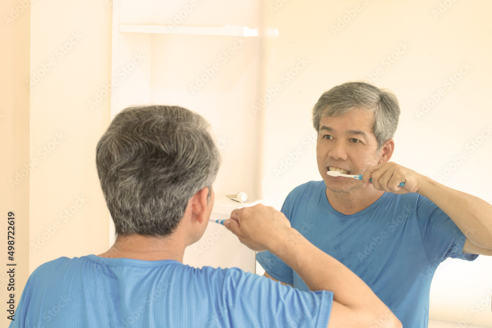 Smiling mature man brushing teeth in bathroom. Happy middle aged looking in mirror while using toothbrush with whitening toothpaste. guy cleaning teeth in the morning time. Smiling mature man brushing teeth in bathroom. Happy middle aged looking in mirror while using toothbrush with whitening toothpaste. guy cleaning teeth in the morning time.