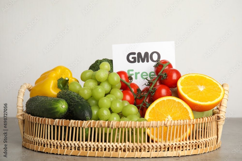 Tasty fresh GMO free products and paper card on grey table against light background