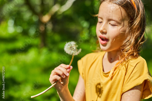 Adorable little girl blowing on a dandelion on a sunny summer day
