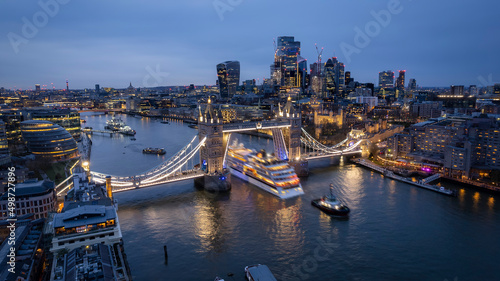 Aerial view of the skyline of London with a motion blurred cruise ship passing under the lifted Tower Bridge during dusk, England
