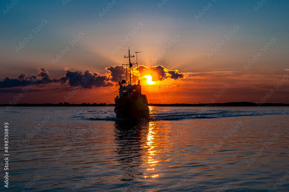 River at sunset with a small boat, dark blue sky, dramatic clouds and sun reflection on the water