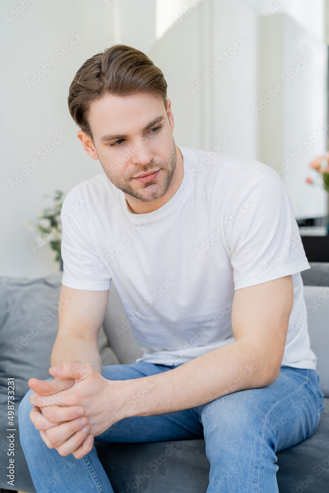 young man in white t-shirt sitting with clenched hands in living room. young man in white t-shirt sitting with clenched hands in living room.