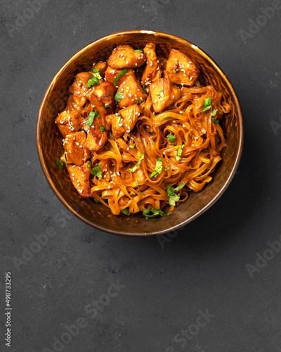 Udon noodles with chicken in teriyaki sauce in a brown bowl on a dark gray culinary background 