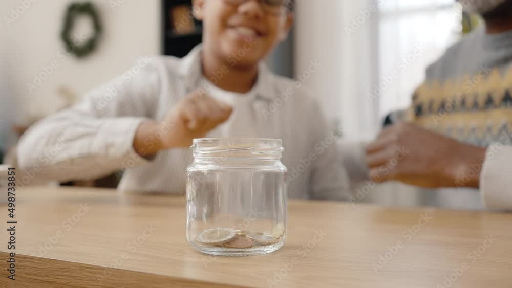 Financial education for kids. Unrecognizable african american boy and grandfather putting coins into jar, saving money Financial education for kids. Unrecognizable african american boy and grandfather putting coins into jar, saving money