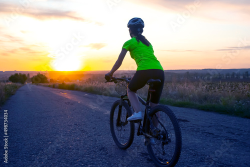 Beautiful woman cyclist riding a bike on the road towards the sunset.